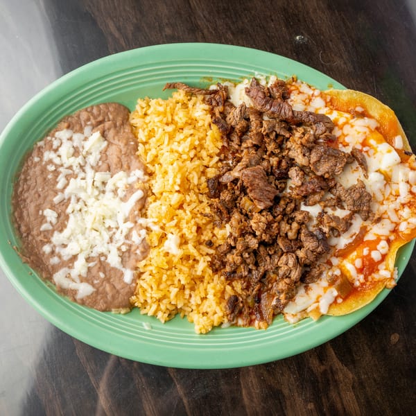 A green plate with refried beans, yellow rice, and carne asada with melted cheese.