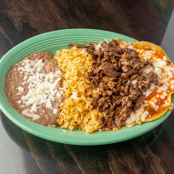 A green plate holds refried beans with cheese, yellow rice, and chopped meat over cheesy enchiladas.