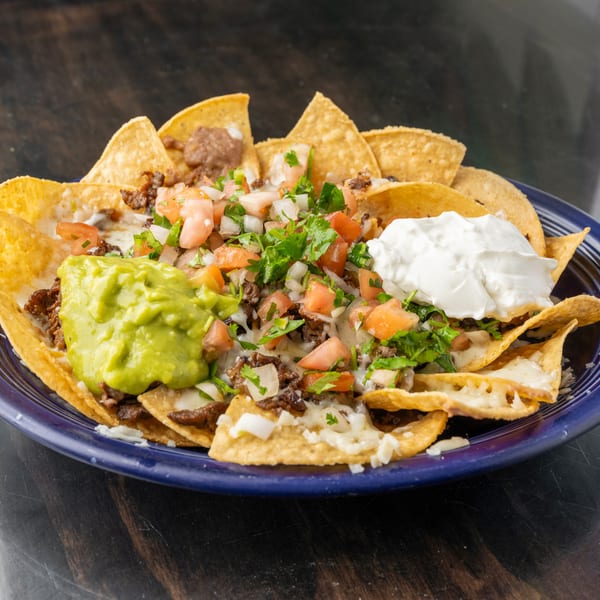 A blue plate of nachos with meat, cheese, pico de gallo, guacamole, and sour cream.