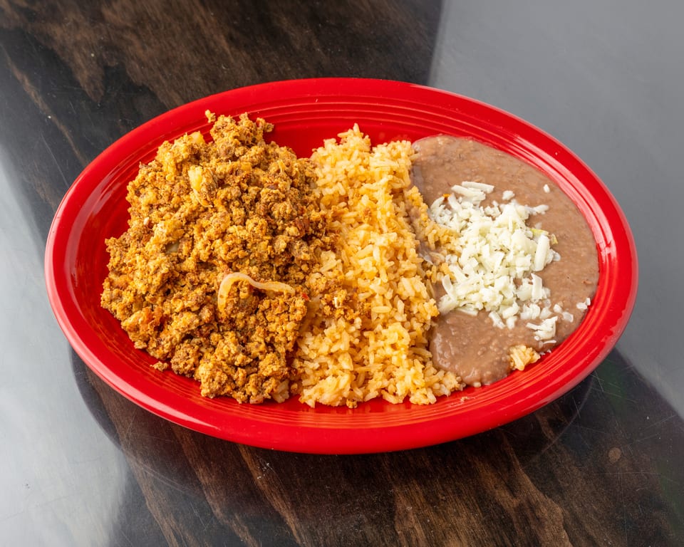 Scrambled eggs with chorizo, rice, and refried beans topped with cheese on a red plate.