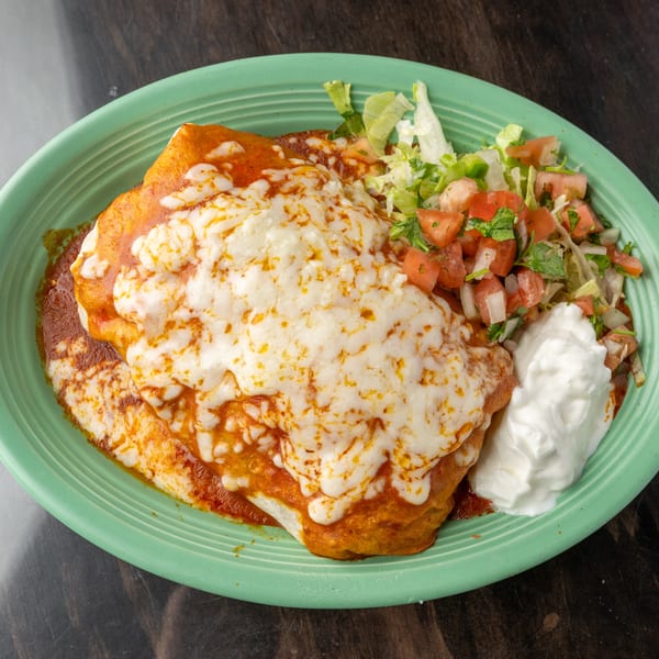 A cheesy burrito covered in red sauce, with a side of lettuce, pico de gallo, and sour cream.