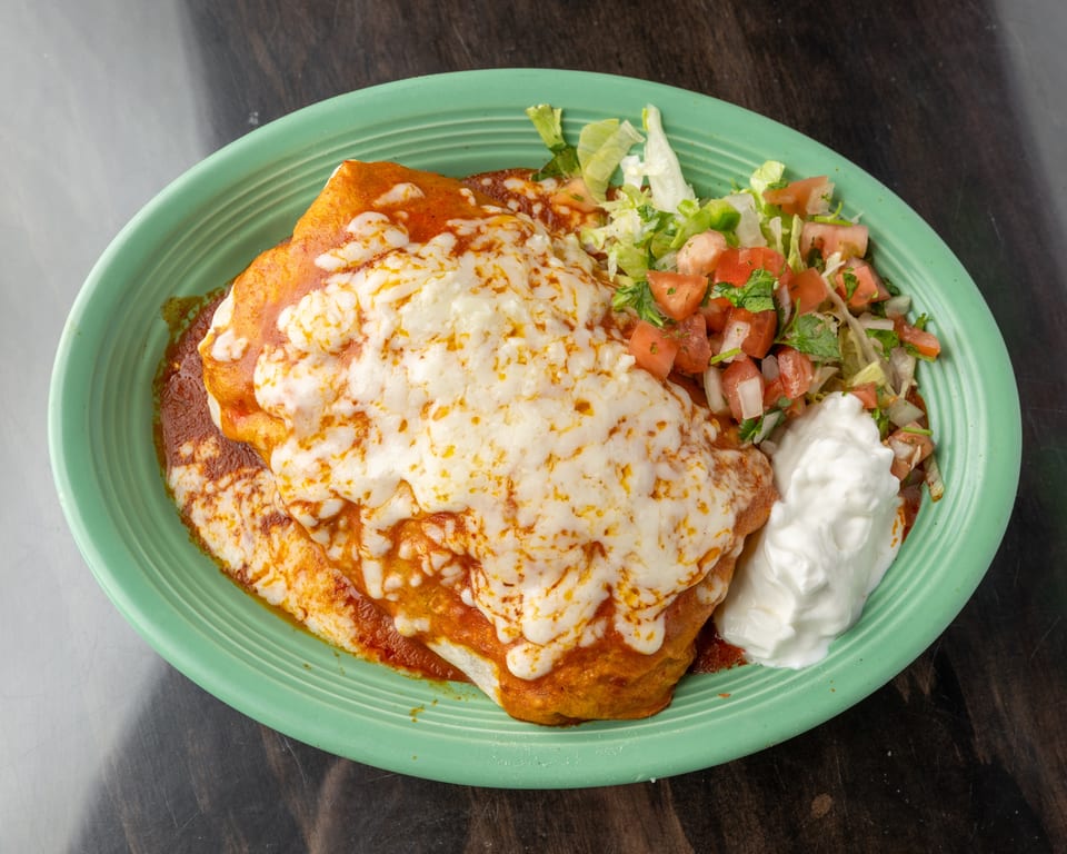 A cheesy burrito covered in red sauce, with a side of lettuce, pico de gallo, and sour cream.