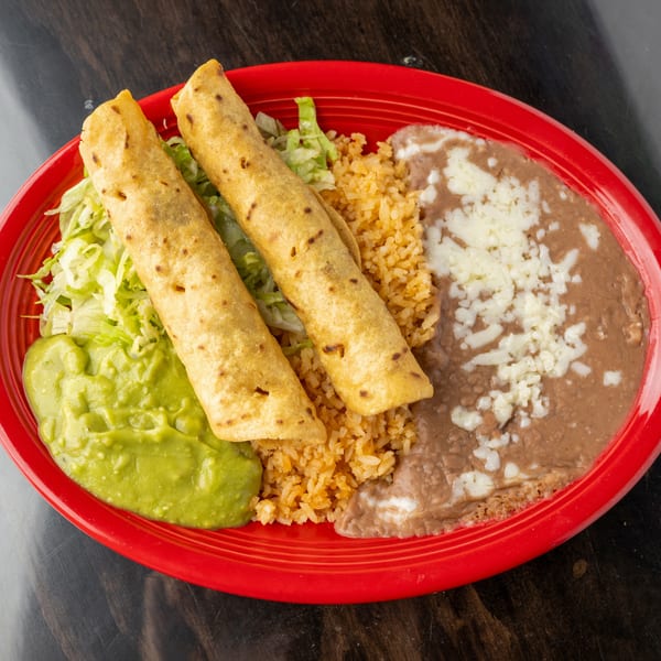 Two golden taquitos with shredded lettuce, guacamole, rice, and refried beans with cheese on a red plate.