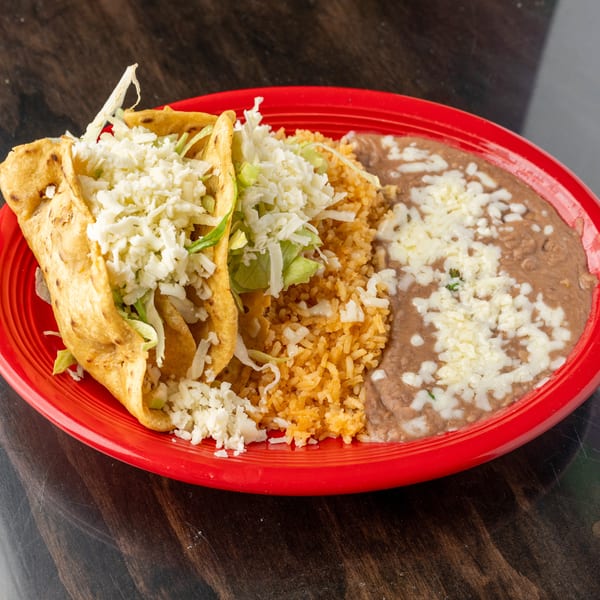 Two crispy tacos with lettuce and cheese, served with rice and refried beans on a red plate.
