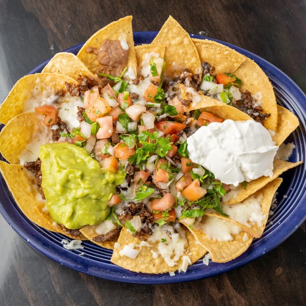 A blue plate of nachos with melted cheese, ground beef, pico de gallo, guacamole, and sour cream.